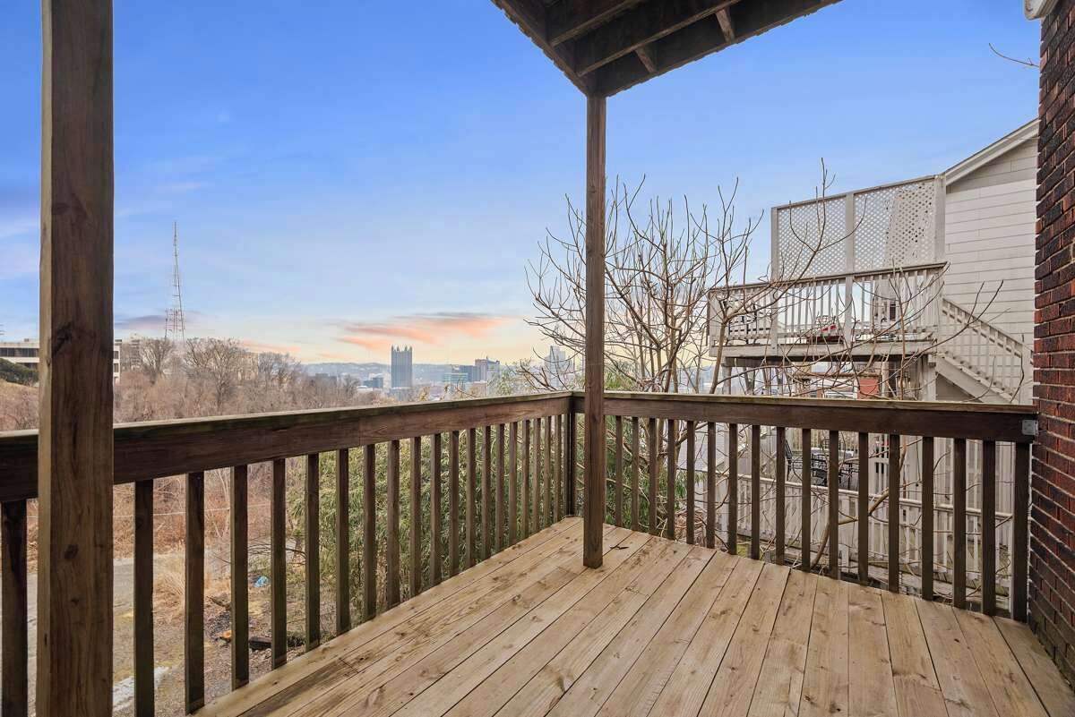 A wooden deck with a view of a city skyline and a building with a metal fence.