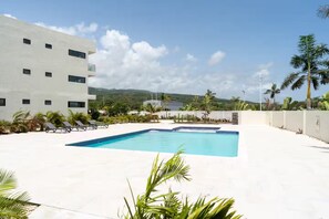 A swimming pool with lounge chairs, a white building, and palm trees. - Paradisiac Euphoria~ Beach Access~Pool~24hr Gated (St. Ann Parish)