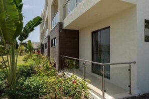 A modern building with a balcony, surrounded by lush greenery and flowering plants. - Paradisiac Euphoria~ Beach Access~Pool~24hr Gated (St. Ann Parish)