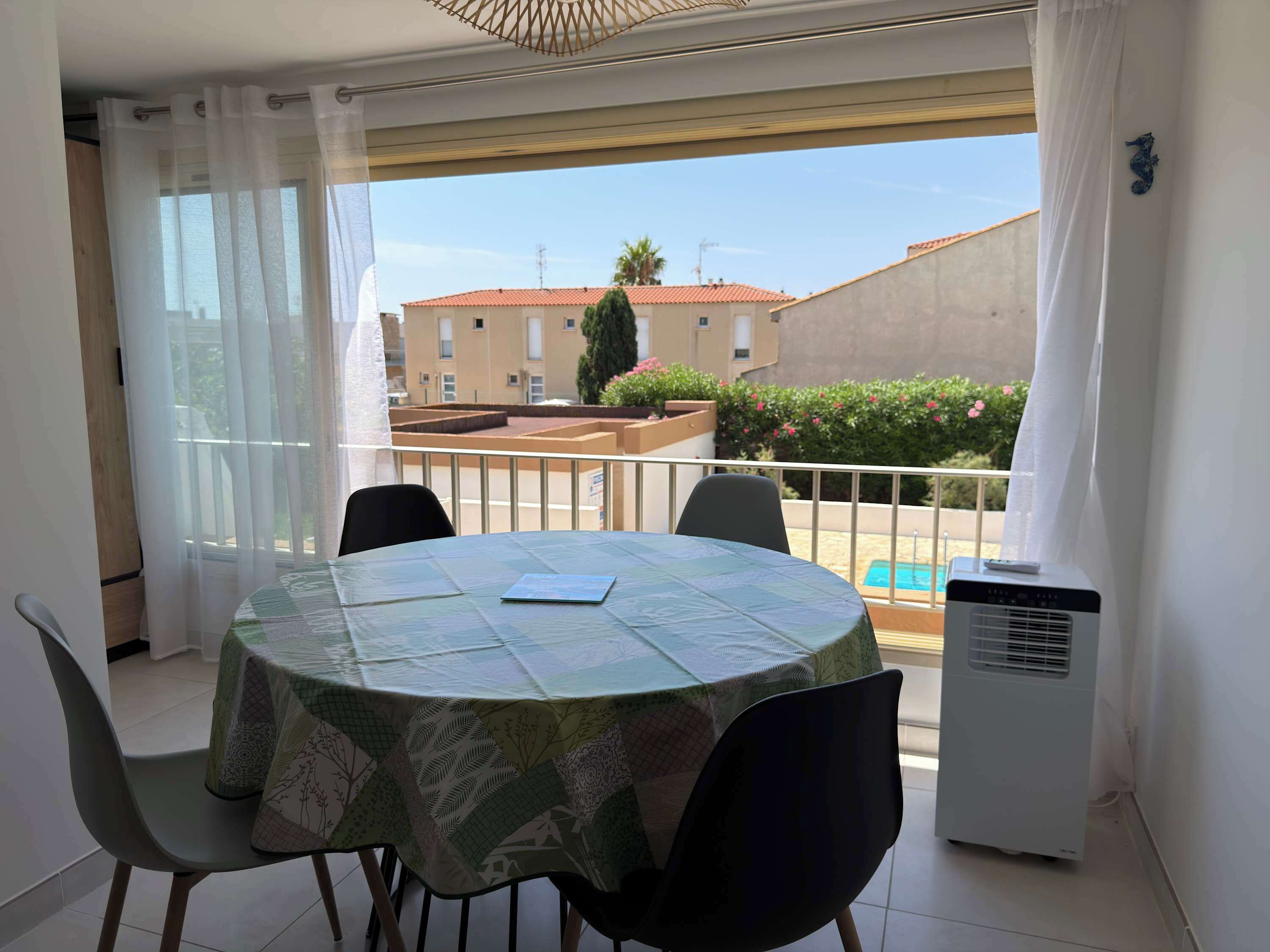 Ein Balkon mit Tisch und Stühlen, im Hintergrund ein Pool und gegenüber die Straße ein Gebäude.