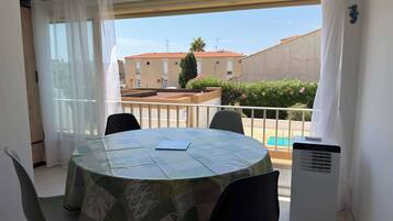 Ein Balkon mit Tisch und Stühlen, im Hintergrund ein Pool und gegenüber die Straße ein Gebäude.