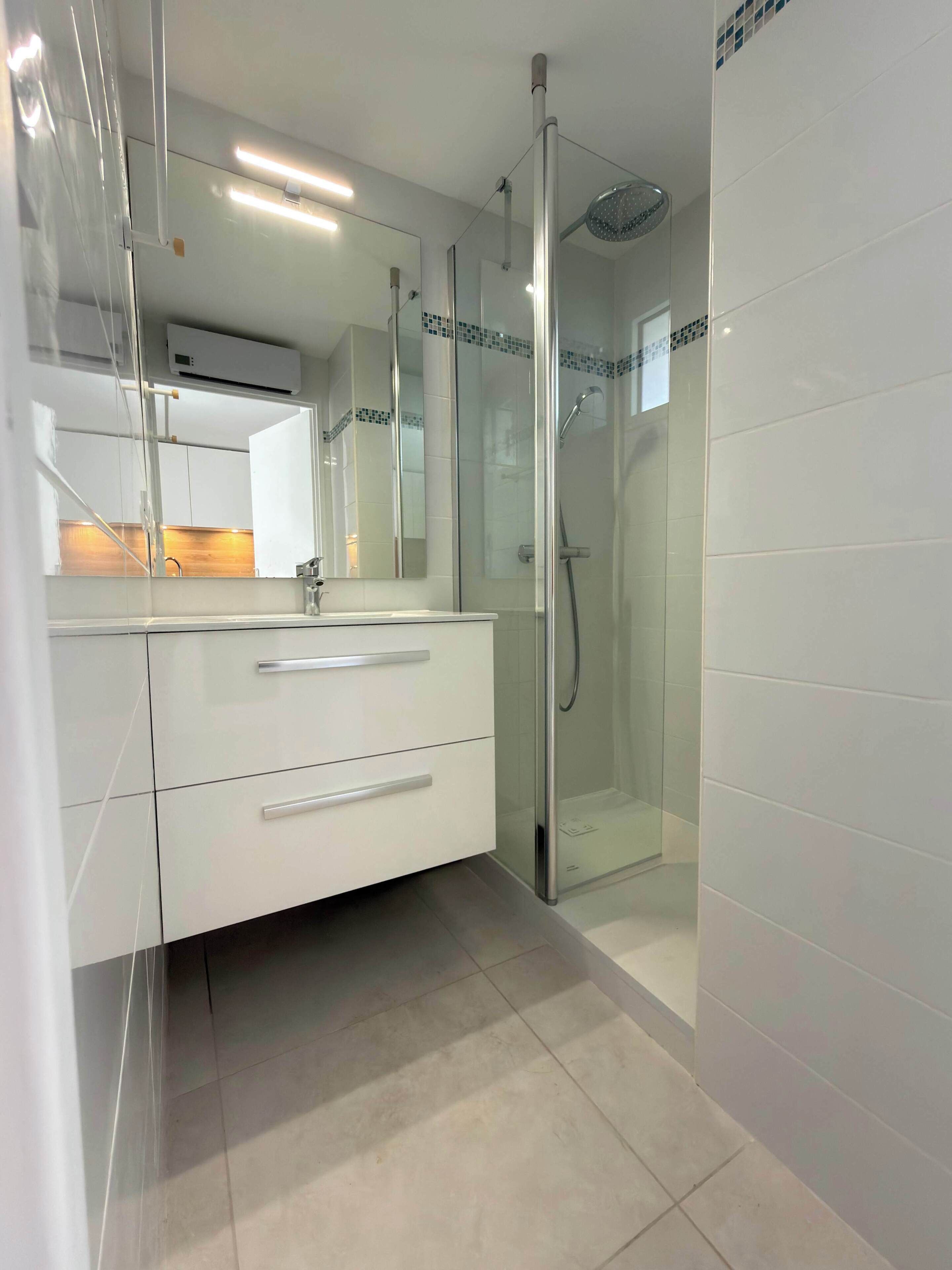 Een moderne badkamer met een douchecabine van glas, een witte wastafel met lades en een spiegel.