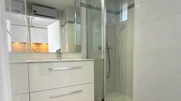 Een moderne badkamer met een douchecabine van glas, een witte wastafel met lades en een spiegel.