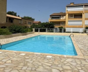 Ein rechteckiger Pool mit Steinrand, umgeben von einer niedrigen Steinmauer und einem Metallzaun.