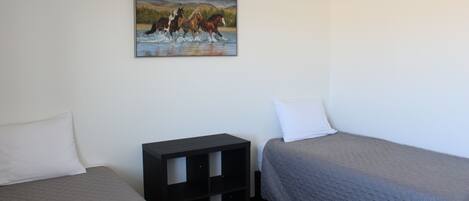 A room with two beds, a painting of horses, and a small black cabinet.