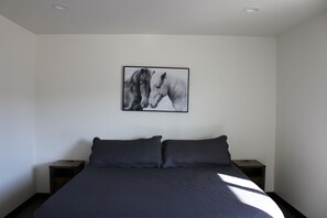 A bedroom with a bed, two nightstands, and a wall-mounted picture of horses.