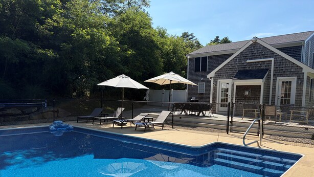 A swimming pool with lounge chairs and umbrellas, surrounded by a fence and trees. - New listing, gorgeous home w/salt water pool in Sandwich, 
10 min from bridge!! (Sandwich)