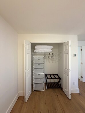 Ein begehbarer Kleiderschrank mit offenen Türen, ausgestattet mit einer weißen Bank, mehreren Stauraumschubladen und Ablageflächen zum Aufhängen.