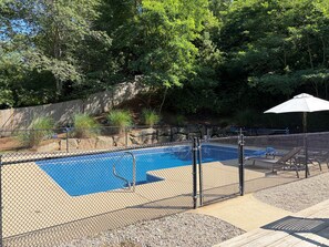 Una piscina amb una tanca metàl·lica, envoltada d'una zona boscosa i un pont de fusta.
