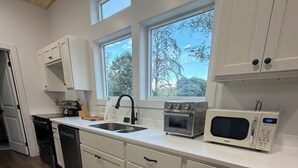 A modern kitchen with white cabinets, a stainless steel sink, a microwave, and a built-in oven. - Modern New Cabin in East TN. Near Cherokee Lake and 1 hr to Pigeon Forge (Bean Station)