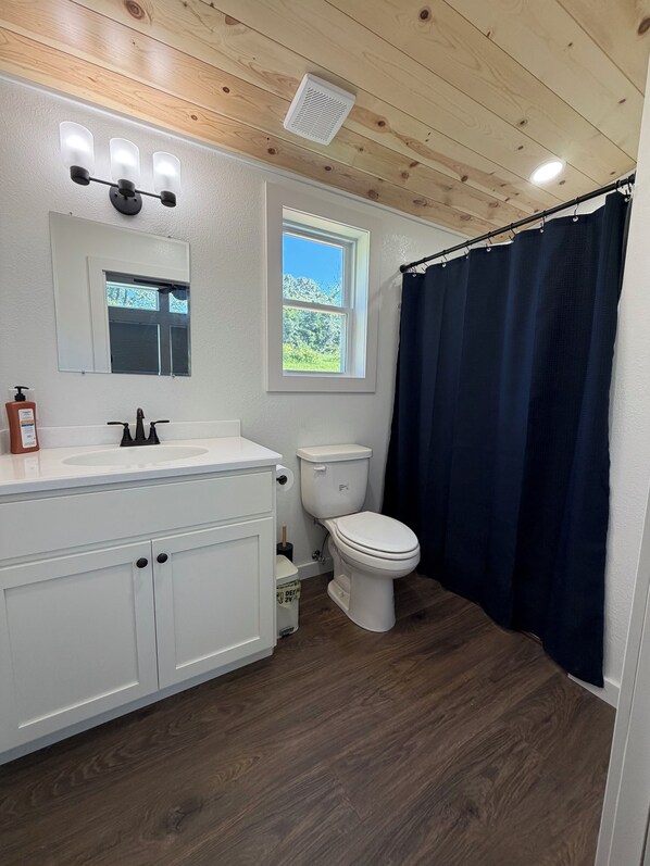 Un baño con tocador blanco, inodoro, ventana y cortina de ducha.