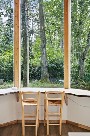 A room with two wooden chairs facing a large window overlooking a forest.