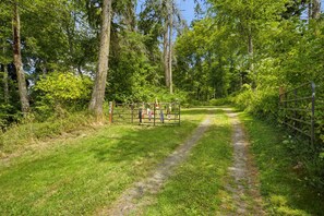A narrow forest path with a metal gate and a signpost.