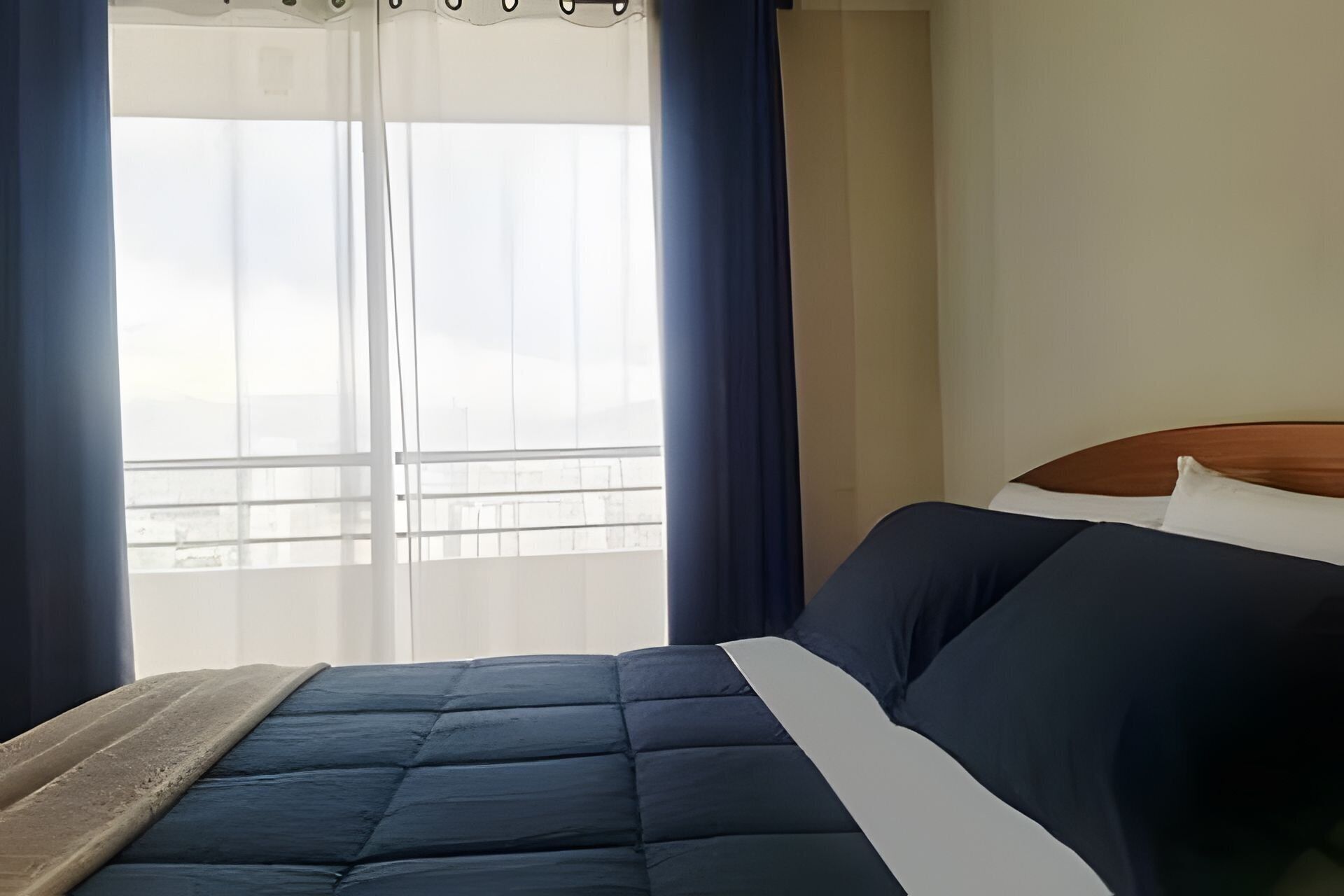 A hotel room with a bed, a window with curtains, and a view of a balcony.