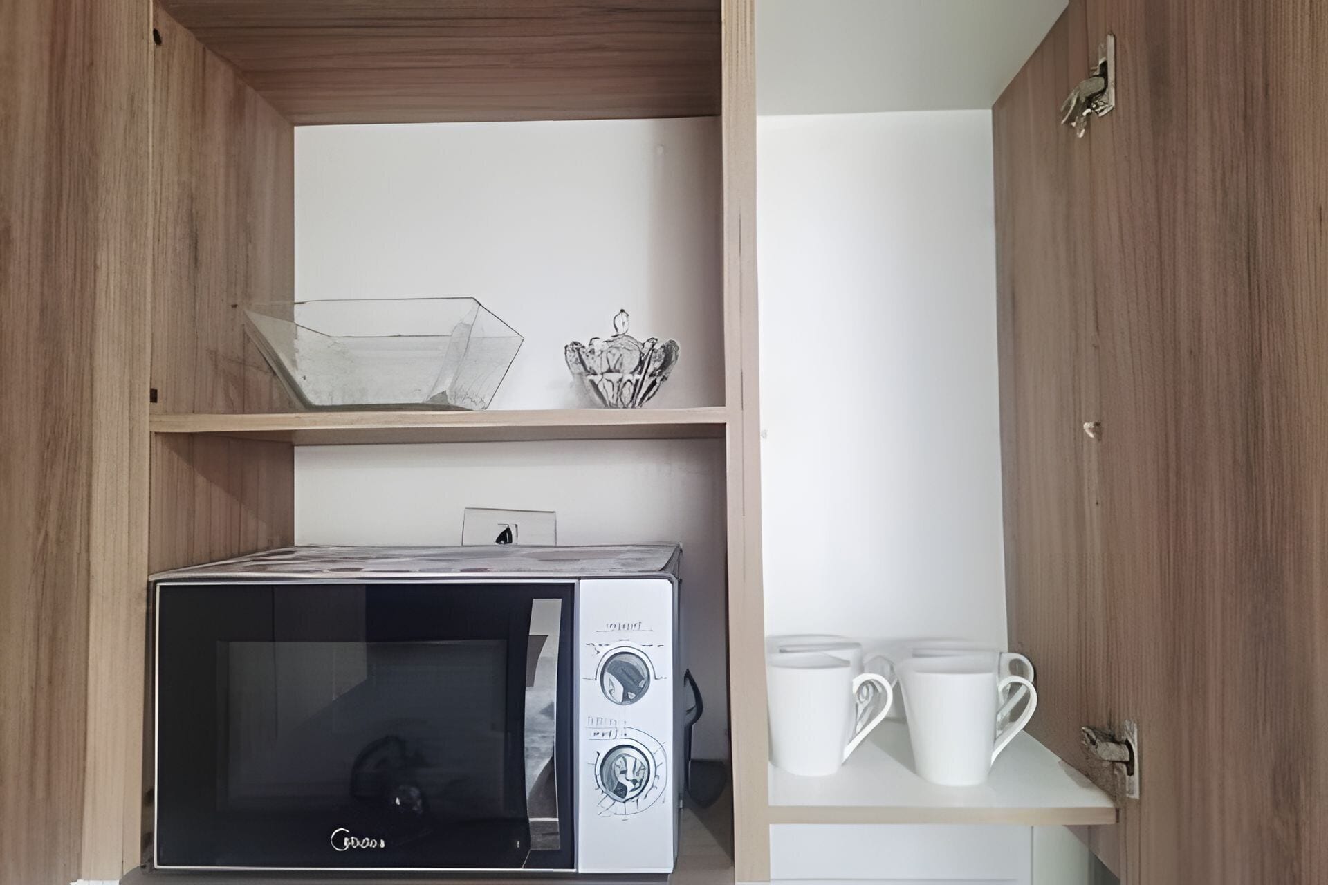 A kitchen with a microwave, a kettle, and a shelf with cups.