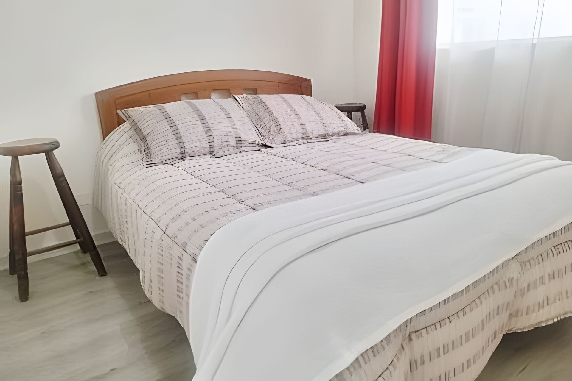 Un lit avec une tête de lit en bois, deux oreillers, un couvre-lit blanc et un rideau rouge.