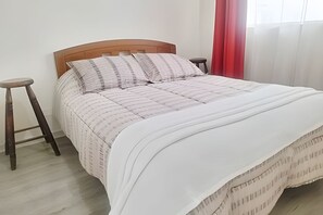 A bed with a wooden headboard, two pillows, a white bedspread, and a red curtain.