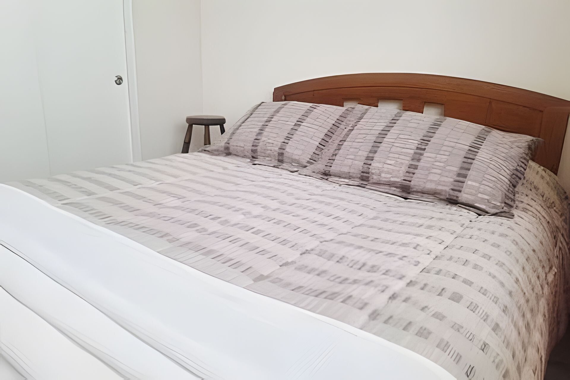 Una cama con una colcha estampada y dos almohadas, un cabecero de madera y una mesita de noche con una silla.
