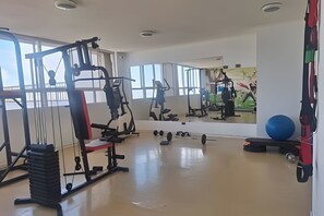 Kuntosali, jossa on monenlaisia kuntoiluvälineitä, suuri peili ja näkymä ulos.