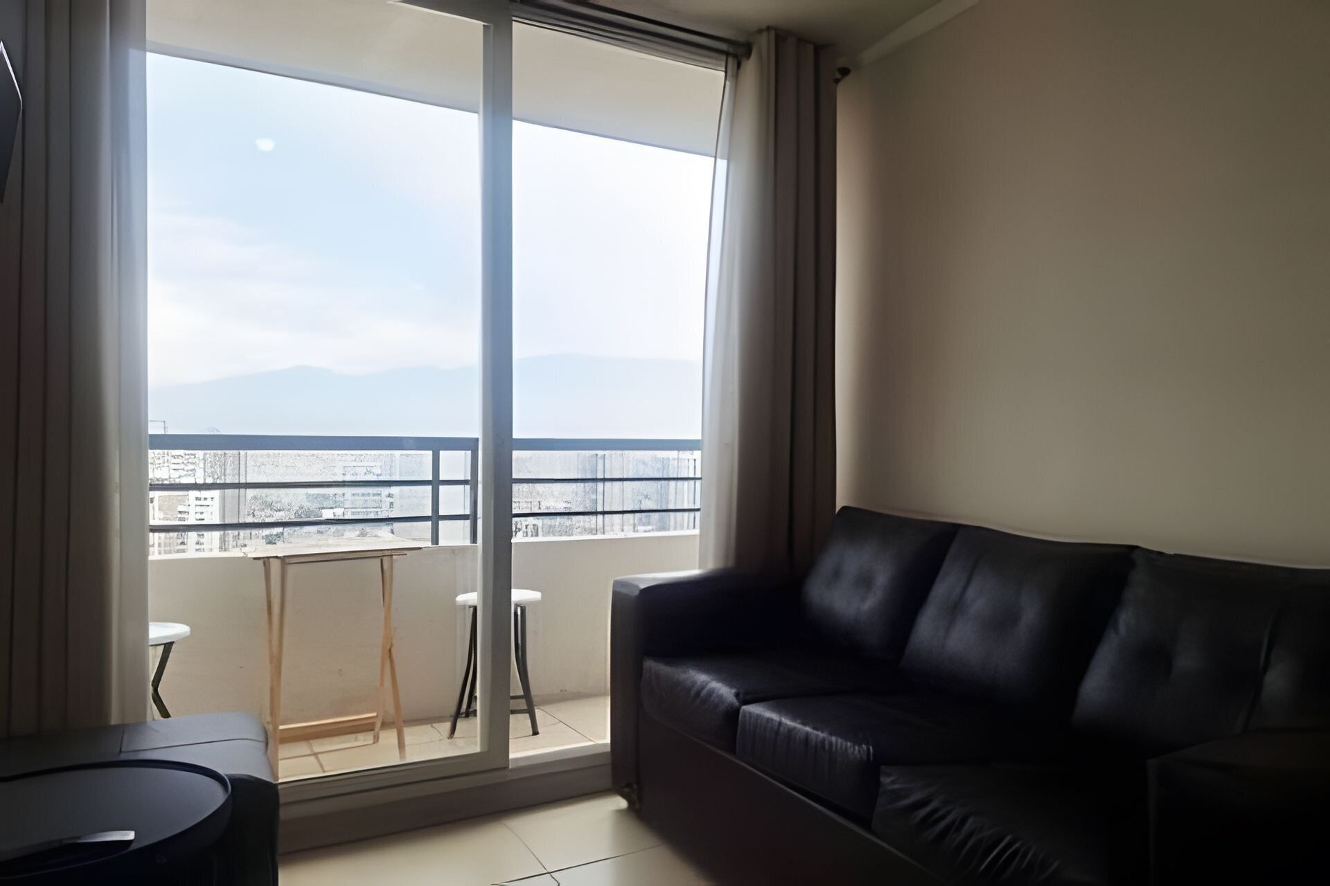 Una habitación con un sofá de cuero negro, una mesita y vistas a un balcón a través de un ventanal grande.