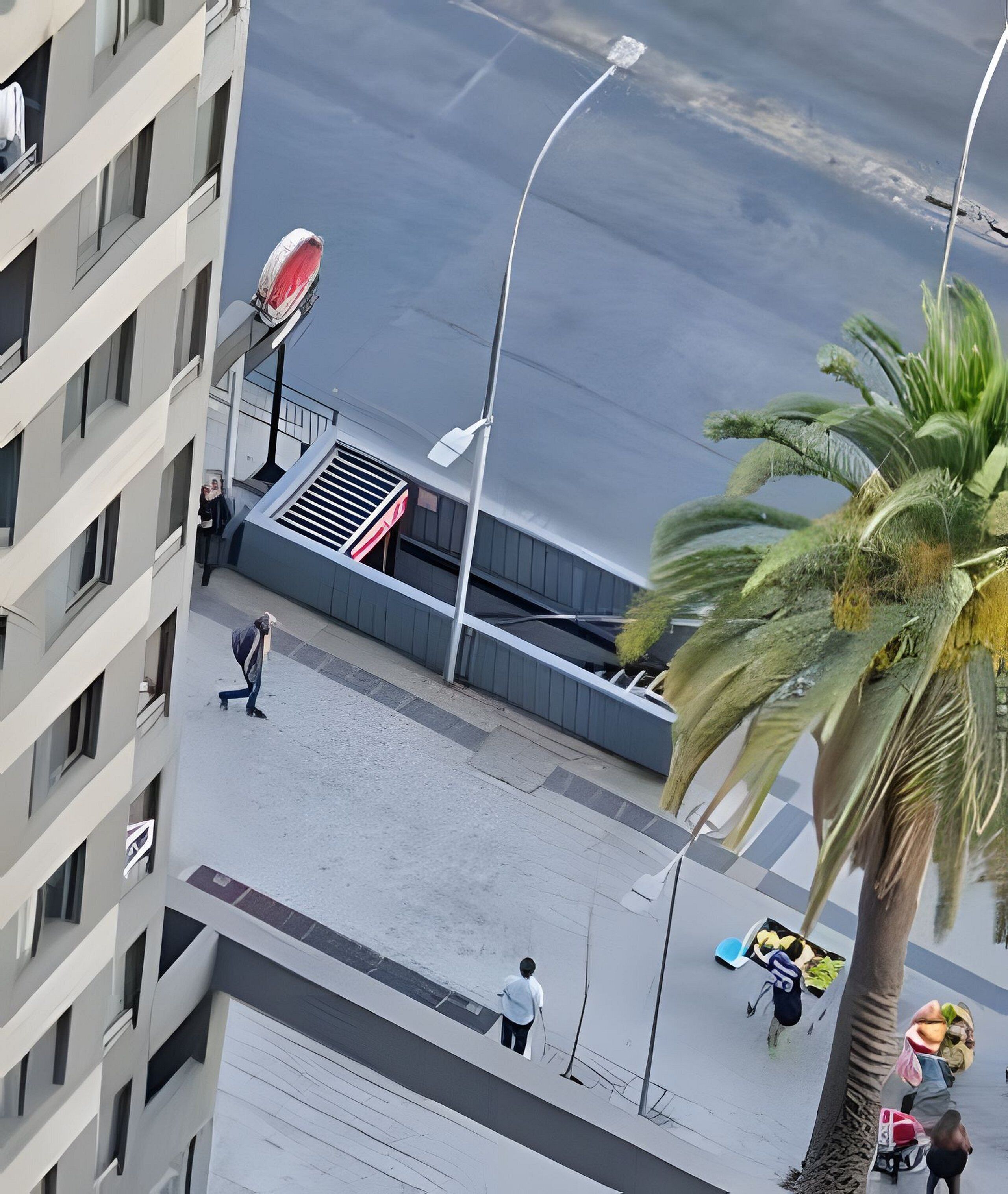 A multi-story building with balconies, a pedestrian walkway, and a palm tree.
