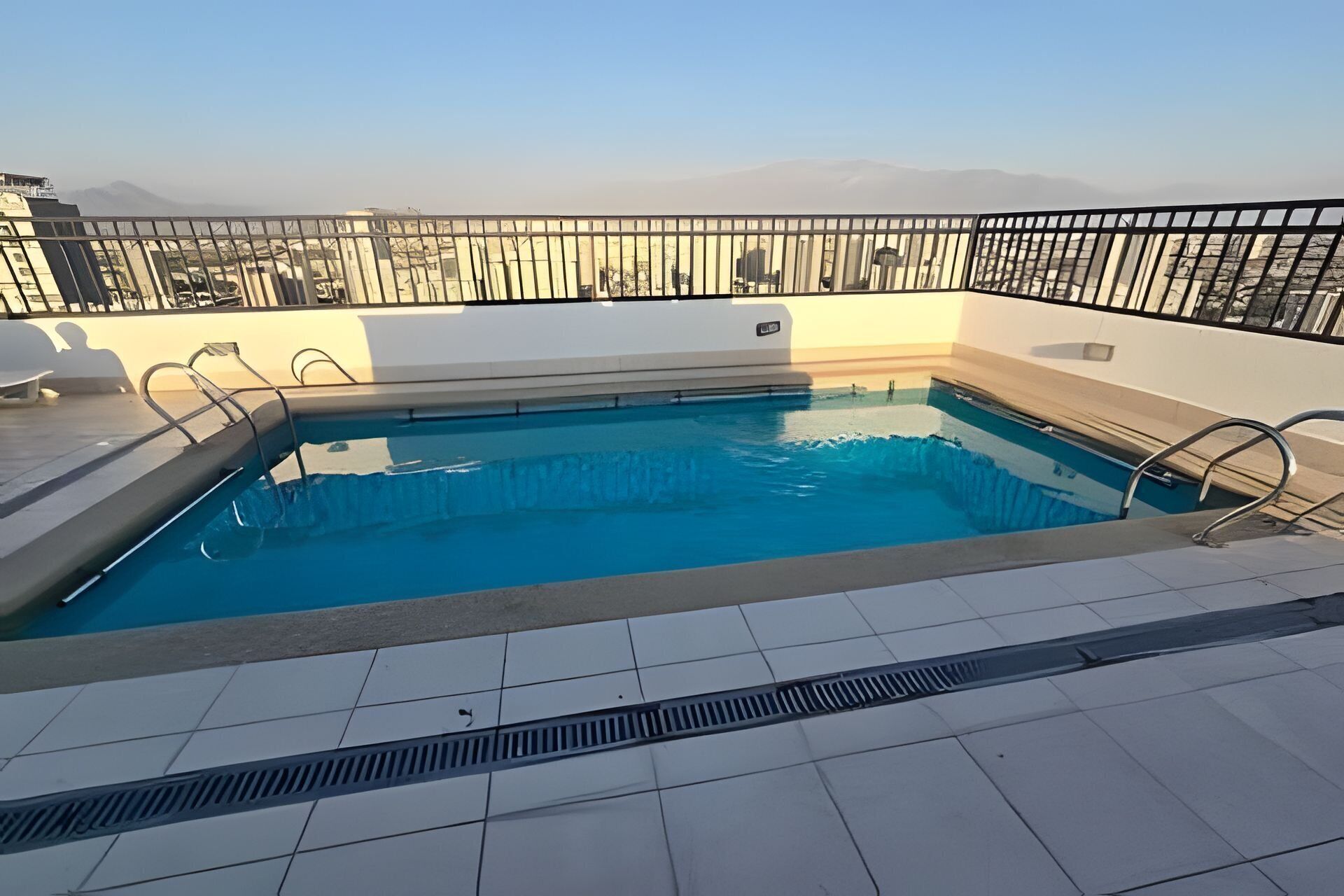 Une piscine sur le toit, dotée d’une rambarde en métal, d’une eau d’un bleu limpide et offrant une vue sur les montagnes lointaines.