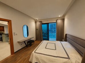 A modern hotel room with a large bed, a desk, a mirror, and a view of the city through the window. - 22nd Fl Damac Tower - 1 BedRoom Apt with Balcony (Amman)