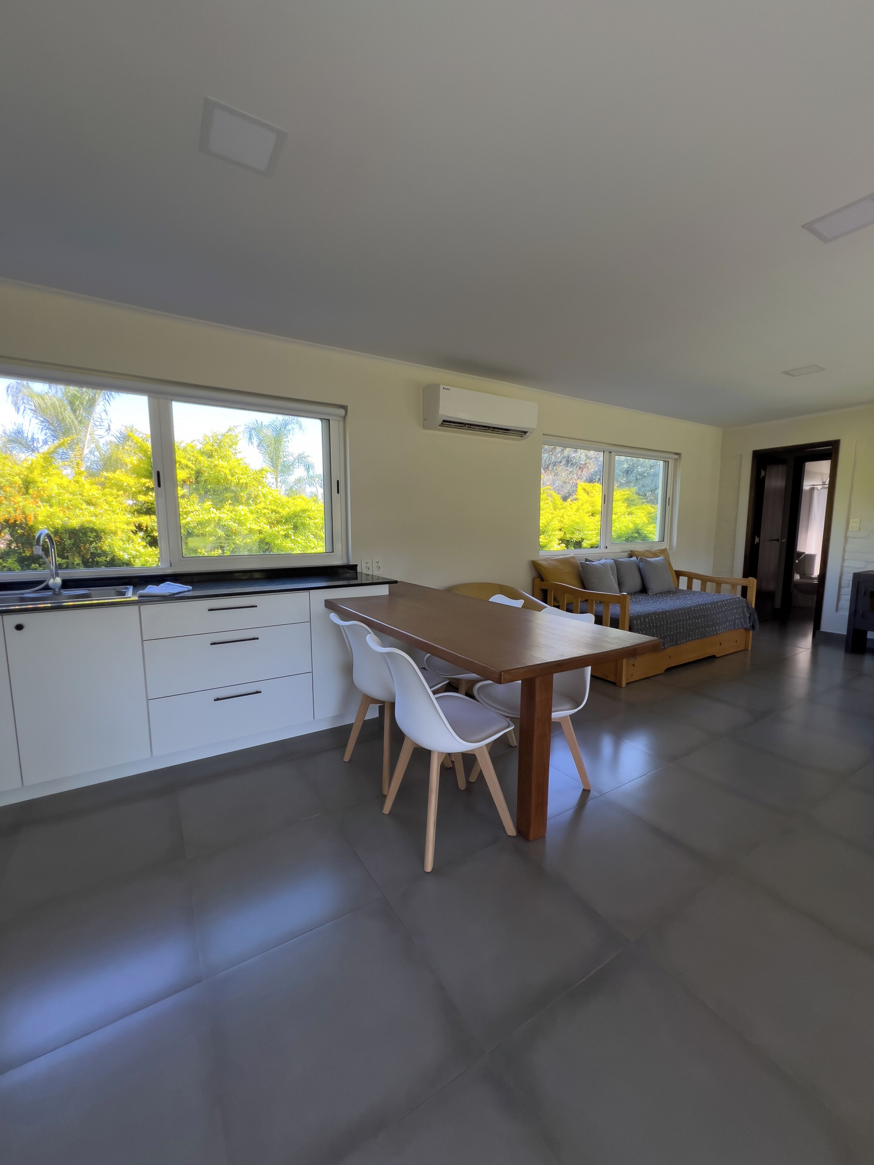 A modern kitchen with white cabinets, a wooden dining table, and a sofa with cushions.