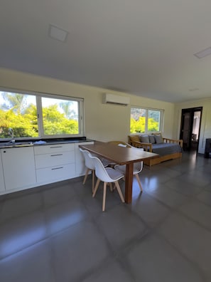 A modern kitchen with white cabinets, a wooden dining table, and a sofa with cushions.