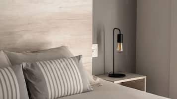 A bed with striped pillows, a wooden headboard, a bedside table with a lamp, and a wall switch.