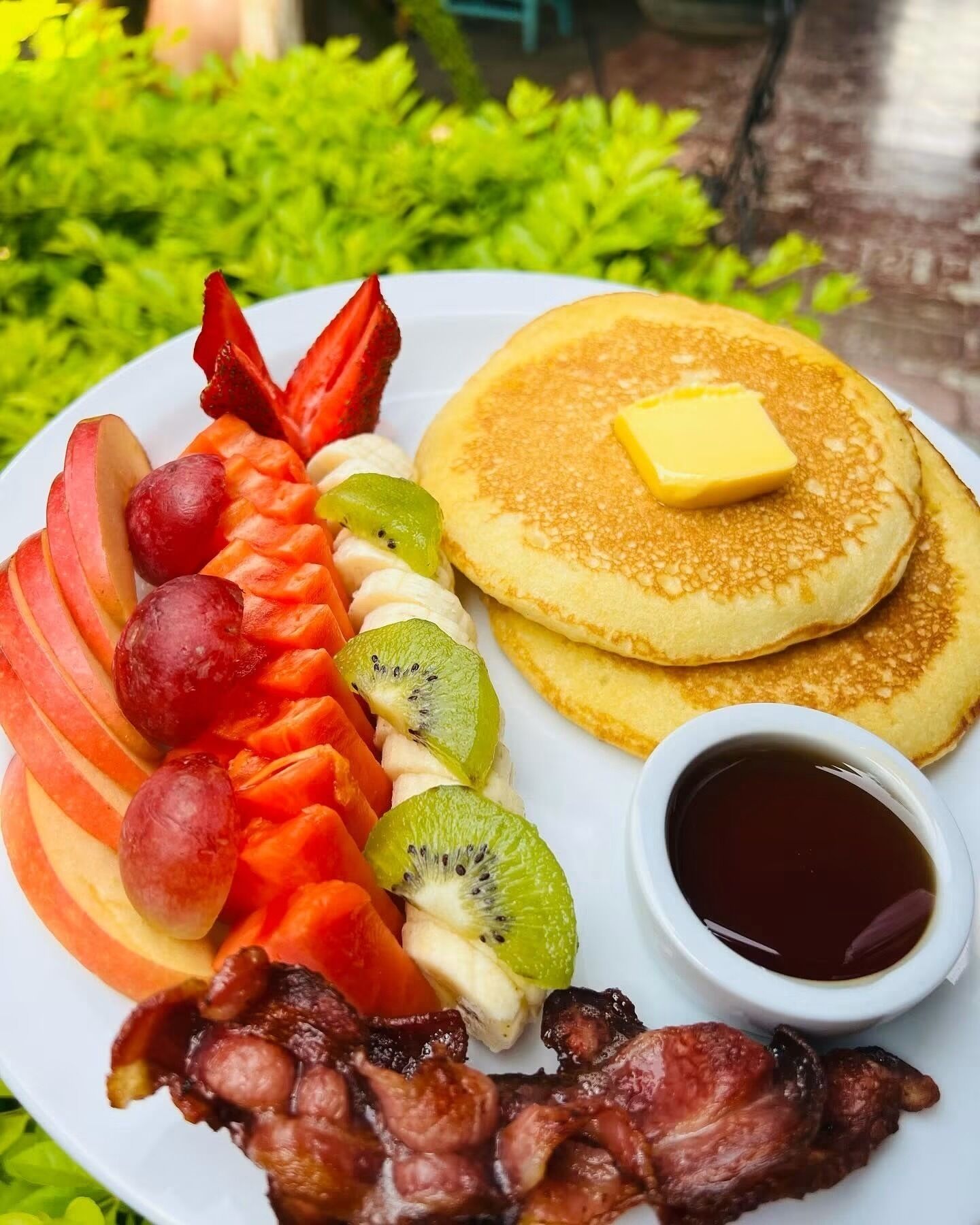 Prato de café da manhã com panquecas, bacon, frutas e xarope.