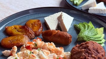 A plate with scrambled eggs, plantains, a sausage, avocado slices, and a meat patty.