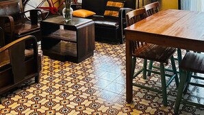 Een kamer met een houten eettafel, een bank met kussens, een fiets, een tafeltje met een bloemenvaas, en een vloer met een patroon.
