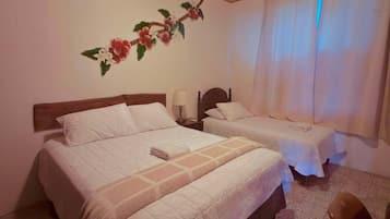 Ein Hotelzimmer mit zwei Betten, einem Nachttisch, einer Lampe, einem Sessel und einer Wand mit floralem Dekor.