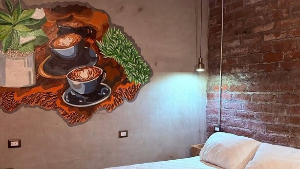 Een slaapkamer met een bed, muurschildering, bakstenen muur en een hanglamp.