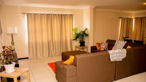 Ein Wohnzimmer mit einem braunen Sofa, einem kleinen Tisch, einer Lampe und einem Blumentopf.