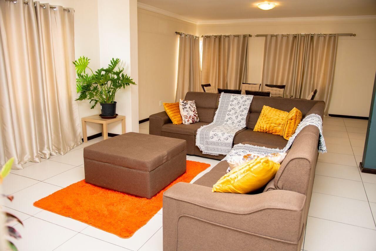 A living room with a brown sofa, orange rug, and a potted plant.