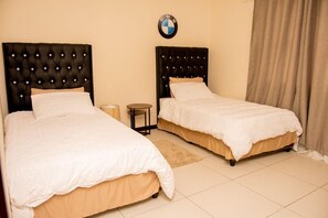 A hotel room with two beds, a BMW logo on the wall, and a curtain on the right. - Home Sweet Home (Swakopmund)