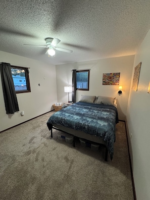A bedroom with a bed, a ceiling fan, a nightstand with a lamp, a window with curtains, and a wall-mounted artwork. - Serene 3-bedroom house in Legendary Sturgis (Sturgis)
