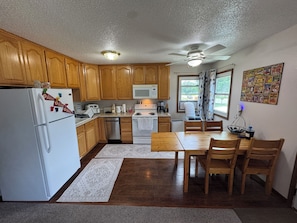 A kitchen with wooden cabinets, a white refrigerator, a microwave, a stove, and a dining table with chairs. - Serene 3-bedroom house in Legendary Sturgis (Sturgis)