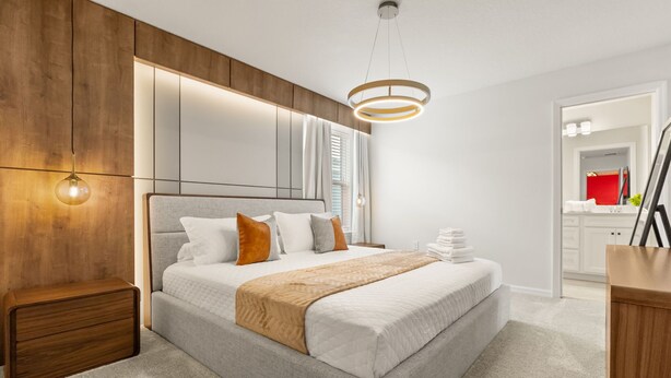 Ein modernes Schlafzimmer mit einem Bett, Nachttischen, einer Pendelleuchte und einem im Hintergrund sichtbaren Badezimmer.