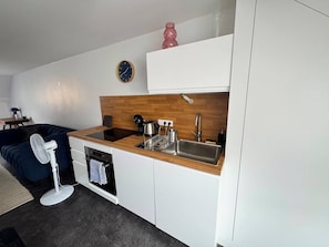 A compact kitchen with a wooden countertop, a sink, a kettle, and a clock on the wall. - Blue Pink | Cozy Apartment in Championnet (Grenoble)