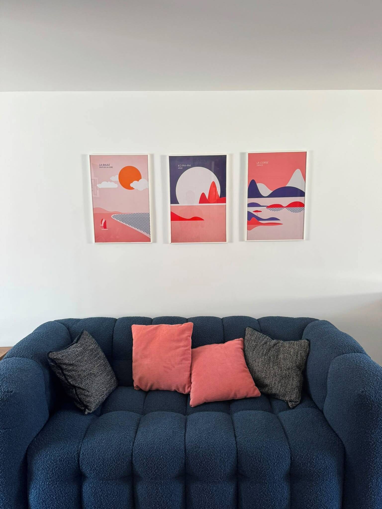 A blue sofa with three cushions and three framed artworks on the wall.