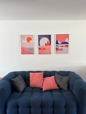 A blue sofa with three cushions and three framed artworks on the wall. - Blue Pink | Cozy Apartment in Championnet (Grenoble)