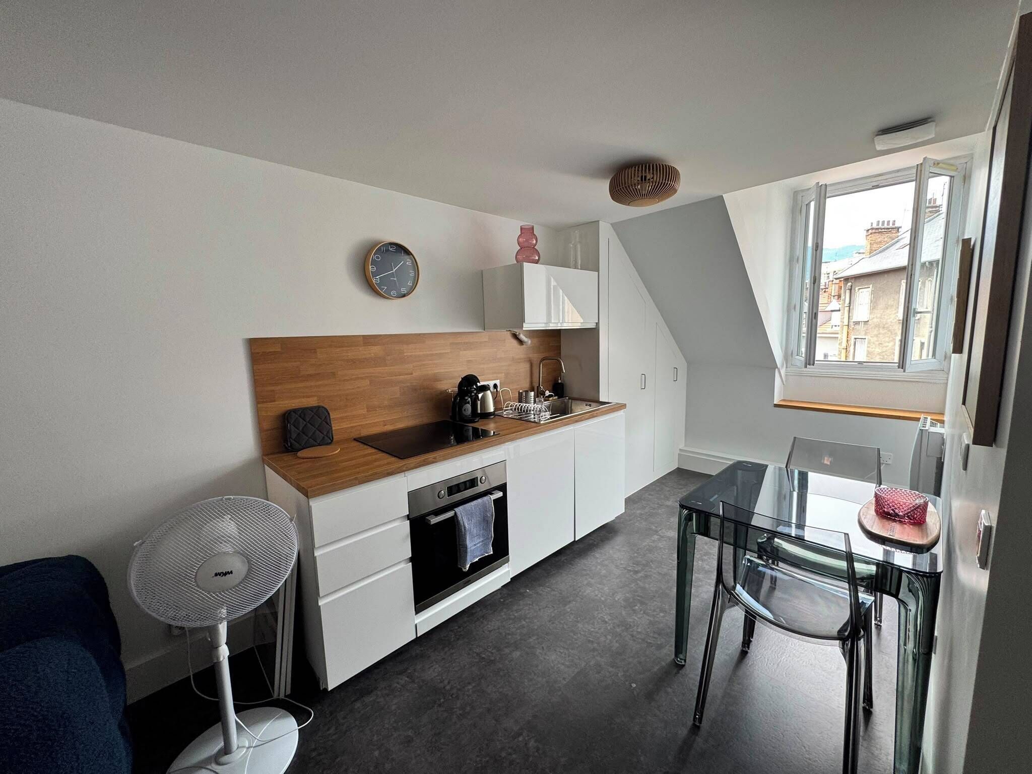 A compact kitchen with a wooden countertop, a built-in oven, and a small dining area with a glass table and chairs.