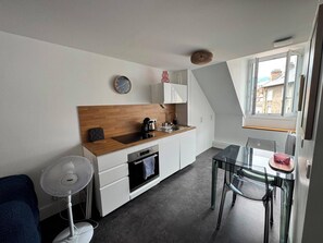 A compact kitchen with a wooden countertop, a built-in oven, and a small dining area with a glass table and chairs. - Blue Pink | Cozy Apartment in Championnet (Grenoble)