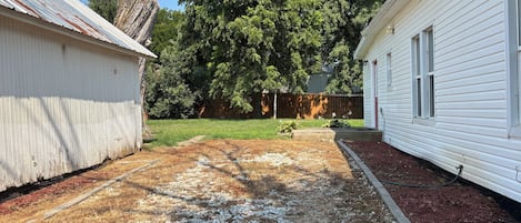A residential property with a grassy yard, a wooden deck, and a white house with a red roof.