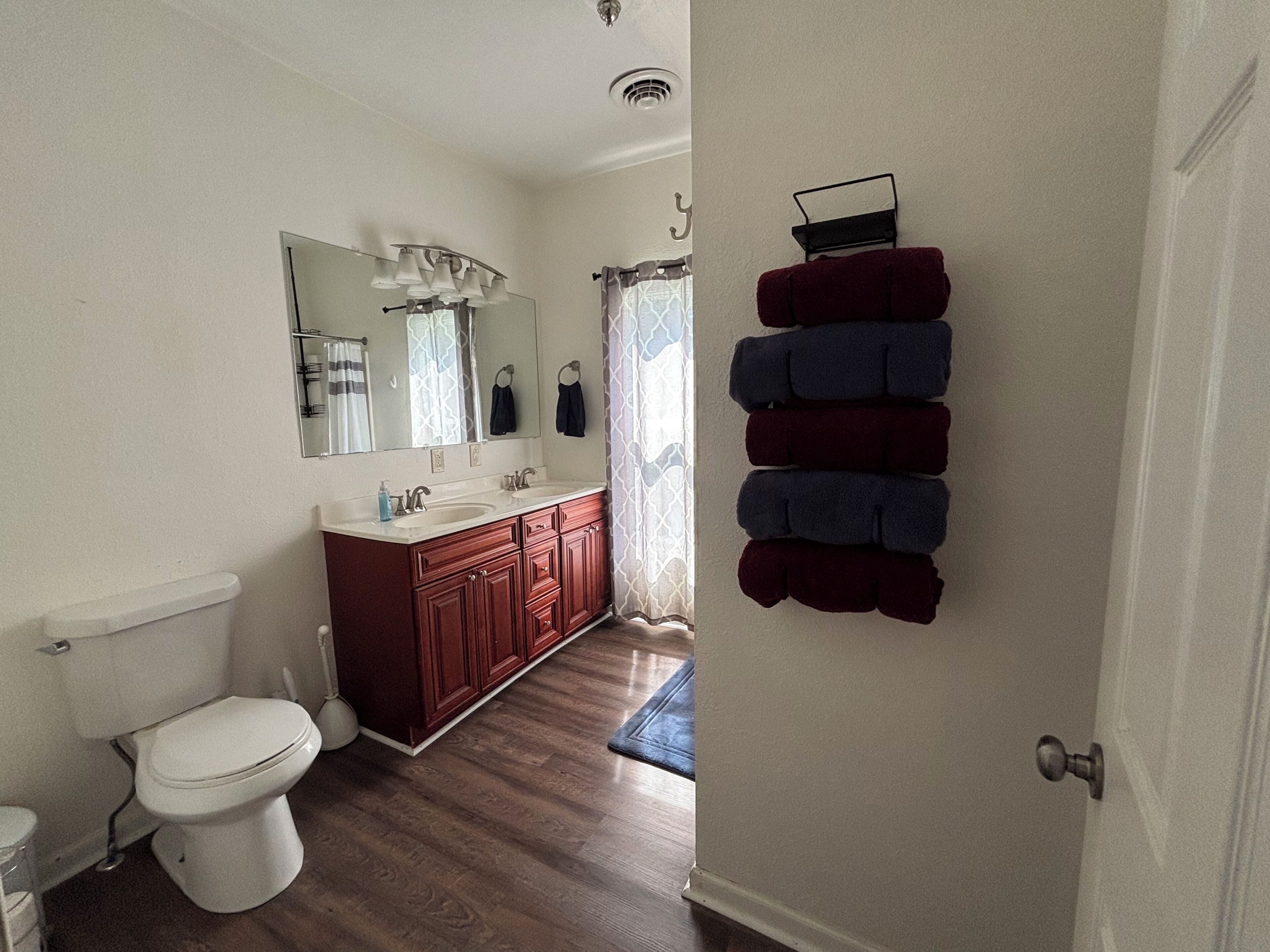 Een badkamer met een wit toilet, een houten wastafelmeubel en een spiegel boven de wastafel.