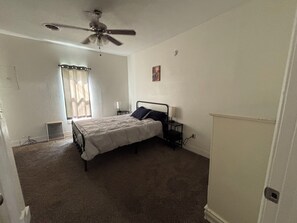 A bedroom with a bed, a nightstand, a ceiling fan, a window with curtains, and a radiator. - Cozy 2-bedroom house in lovely Greentop (Greentop)
