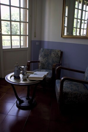A room with a window, a chair, a table with a book and a teapot, and a sofa. - Charming Villa with a Hot Tub in a Pine Forest (Talacchio)